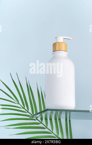 White cosmetic bottle with natural wood pump, ready for branding mockup, placed next to a vibrant green leaf on a reflective glass surface with a tran Stock Photo