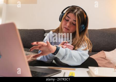 A young woman juggles tasks at home, wearing headphones and using a laptop, with a puzzled expression Stock Photo