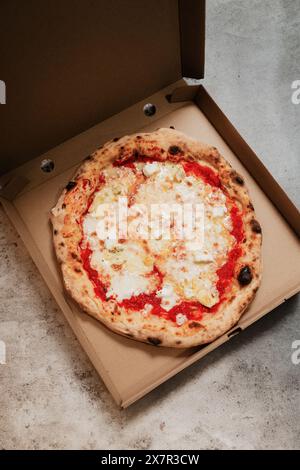 An overhead view of a freshly baked pizza inside a cardboard box, placed on a textured concrete surface, representing takeaway or delivery from a pizz Stock Photo