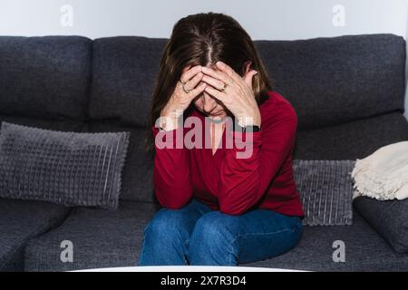 A woman sits on a couch, her face in her hands, symbolizing distress from a hypoglycemia episode Stock Photo