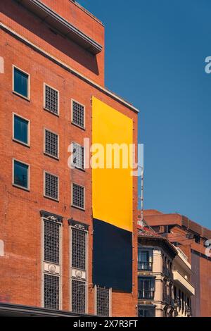 Large empty yellow and black banner on a red brick building against the blue sky, perfect for mockups and advertisements in Madrid Stock Photo