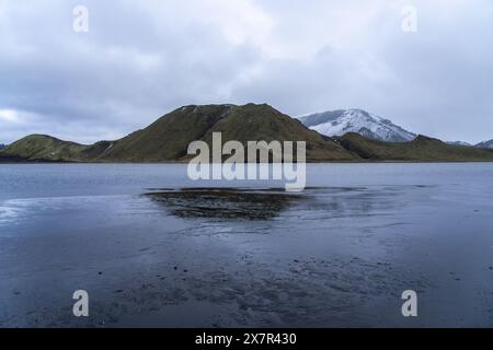 Serene lake surrounded by the green and snowy hills of the Icelandic Highlands under a moody sky Stock Photo