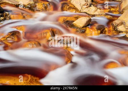 Captivating image showing the vibrant orange waters of the Riotinto River flowing gently over scattered stones, highlighted by a silky smooth effect Stock Photo