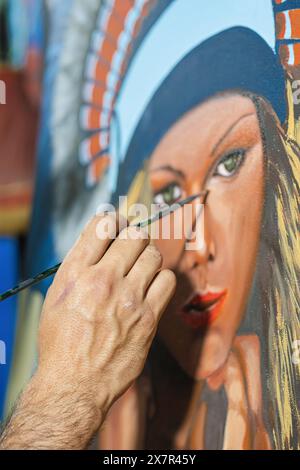 Cropped unrecognizable man's hand expertly adds detail to a vibrant painting of a woman in a sunny art studio. Stock Photo