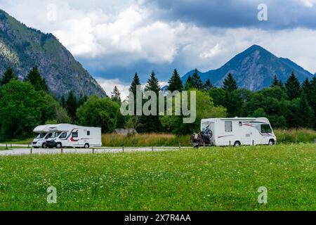 Two white motorhomes with bicycles parked on a grassy clearing, surrounded by the lush beauty of the Italian and Austrian Alps under a cloudy sky Stock Photo