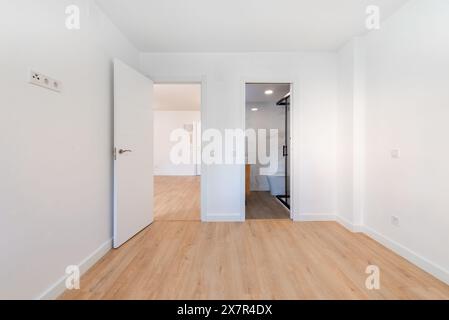 A contemporary empty apartment features a spacious room with polished wooden floors, white walls, and multiple open doors leading to adjacent rooms, e Stock Photo