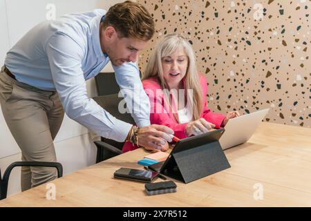 Two professionals collaborate at a wooden table in a chic coworking environment, sharing ideas on digital devices Stock Photo