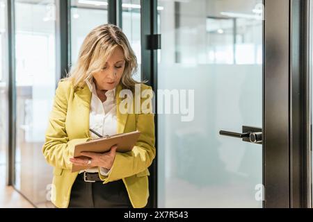 Professional woman in a bright yellow blazer working on her tablet in a well-lit coworking office environment Stock Photo