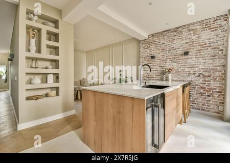 Spacious modern kitchen featuring sleek wooden cabinets and a textured brick wall The room includes a stylish island with built-in sink and open shelv Stock Photo