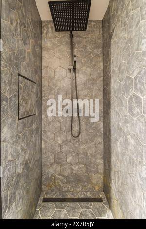 Sleek and contemporary bathroom design featuring a large rain shower head, black fixtures, and a stylish gray stone tiled walls and floor in a varied Stock Photo