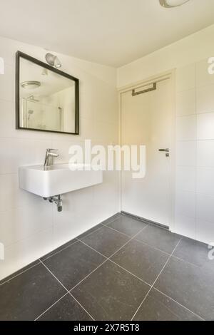 A contemporary bathroom featuring a white rectangular sink, large mirror, and contrasting dark floor tiles, creating a clean and stylish look. Stock Photo