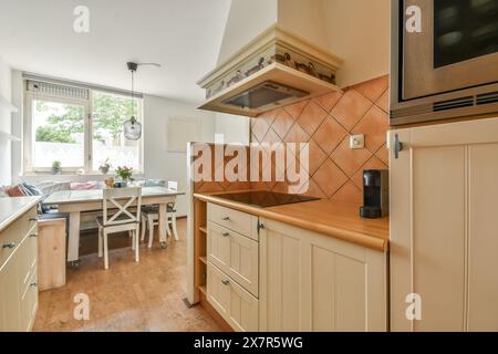 A sunny, well-appointed kitchen space in Sandwijk, Amsterdam, featuring beige cabinetry and diamond-patterned tiles Soft natural light filters through Stock Photo