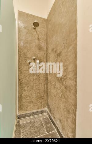 A contemporary shower area with a polished concrete texture on the walls and slate floor tiles, displaying a minimalist aesthetic with modern fixtures Stock Photo