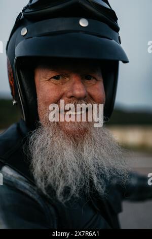 A cheerful elderly male biker wearing a helmet and leather jacket, looking at camera with a friendly smile. Stock Photo