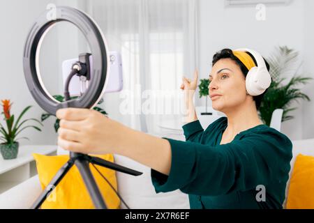 A female influencer engages with her audience while recording a podcast, using a ring light for enhanced video quality, in a bright, modern home setti Stock Photo