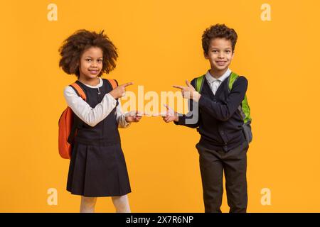 Two Smiling Schoolchildren With Backpacks Pointing at Each Other Stock Photo