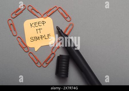 Keep it simple is written on a yellow sticky note on a gray desk. Stock Photo