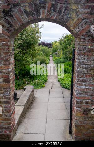 View of a lush garden path through an old brick archway, surrounded by flourishing plants and flowers Stock Photo