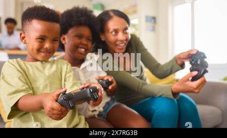 Excited Mother And Children Sitting On Sofa At Home Playing Computer Game Stock Photo