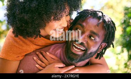 Loving Mid Adult Couple Outdoors In Summer Garden Or Countryside With Man Giving Woman Piggyback Stock Photo