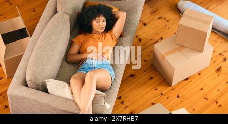 Overhead Shot Of Tired Woman On Break From Unpacking Lying On Sofa In New Home On Moving Day Stock Photo