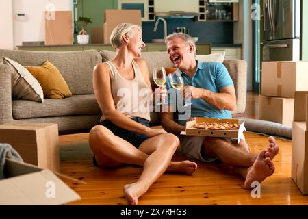 Mature Couple Celebrating In New Home On Moving Day Eating Pizza And Drinking Wine Stock Photo