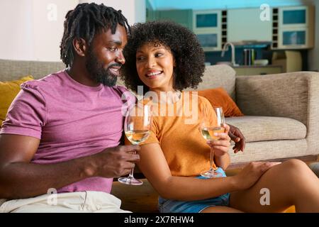 Young Couple Relaxing At Home Sitting On Floor Next To Sofa Drinking Wine Stock Photo
