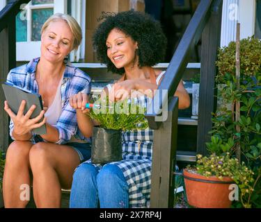 Female Staff With Digital Tablet Sitting On Steps Working In Garden Centre Looking After Plants Stock Photo