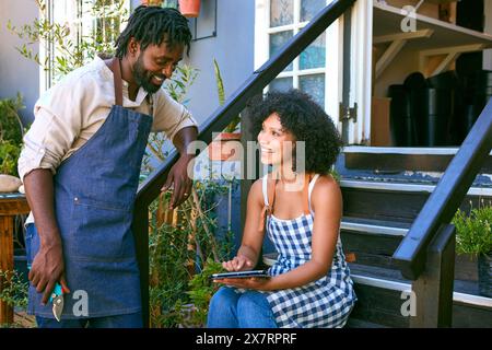 Male And Female Staff With Digital Tablet Sitting On Steps Working In Garden Centre Stock Photo