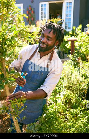 Man Working In Garden Centre Checking And Pruning Plants With Secateurs Stock Photo