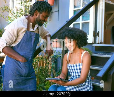 Male And Female Staff With Digital Tablet Sitting On Steps Working In Garden Centre Stock Photo