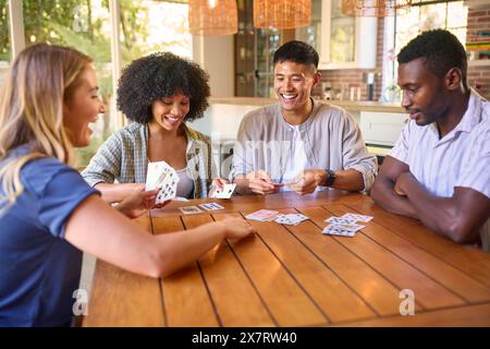 Group Of Multi-Racial Friends Sitting Around Table Playing Game Of Cards At Home Together Stock Photo