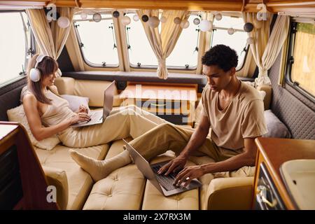 A man and woman sit on a couch, each engrossed in their laptops, with focused expressions. Stock Photo