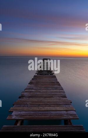 Peaceful sunrise seascape with an old wooden dock leading out into the calm ocean waters Stock Photo