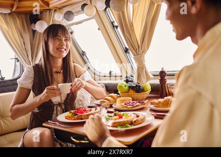 An interracial couple savors a delicious lunch together at a table set with plates of food in a camper van. Stock Photo