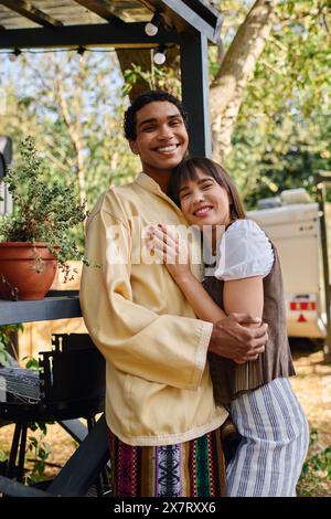 An interracial couple hugs tenderly in front of a lush potted plant, symbolizing their deep connection amidst a natural setting. Stock Photo