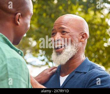Family Shot With Senior Father Talking And Laughing With Adult Son Outdoors In Countryside Stock Photo