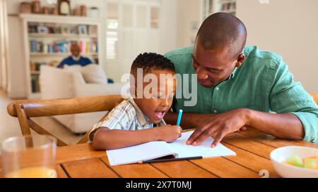 Family Indoors At Home With Father Drawing Picture With Son With Grandparents In Background Stock Photo