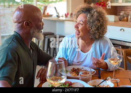 Smiling Senior Couple Enjoying Meal At Home Together And Drinking Glasses Of Wine Stock Photo