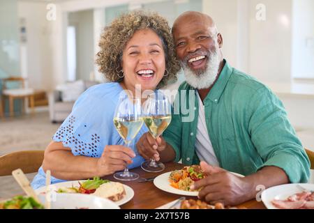 Portrait Of Loving Mature Couple At Home Enjoying Lunch With Wine Together Stock Photo