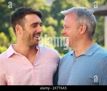 Portrait Of Laughing And Smiling Mature Father With Adult Son Standing Outdoors In Countryside Stock Photo