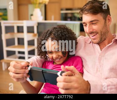 Multi Racial Family With Father And Daughter Playing On Handheld Gaming Device Together Stock Photo