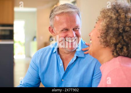 Loving Multi-Racial Mature Couple Sitting On Sofa At Home Laughing And Talking Together Stock Photo