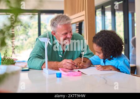Family With Grandfather And Granddaughter Doing Homework On Green Energy With Model Turbine Stock Photo
