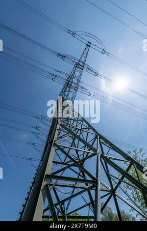 Against the clear blue canvas of the sky, the high voltage pylon stands resolute, accentuating the vital link between technology and nature in our mod Stock Photo