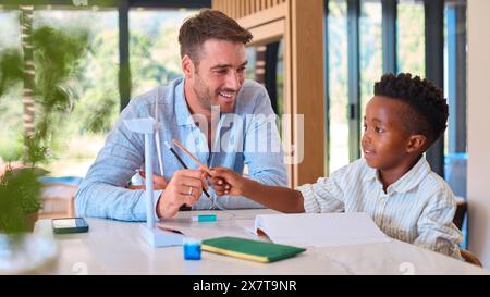 Multi Racial Family With Father And Son Doing Homework On Green Energy With Model Turbine Stock Photo