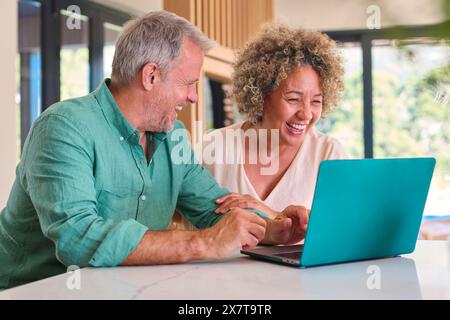 Smiling Multi-Racial Mature Couple At Home Looking At Laptop Together Stock Photo