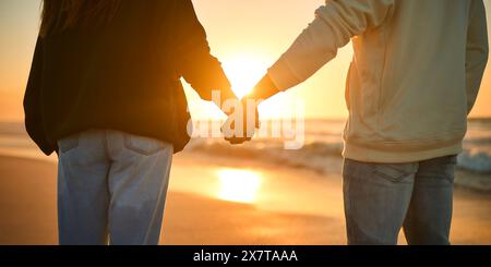 Close Up Of Casually Dressed Loving Young Couple Holding Hands On Beach Shoreline At Sunrise Stock Photo