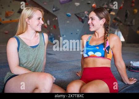 Two Women Taking A Break And Talking By Climbing Wall In Indoor Activity Centre Stock Photo
