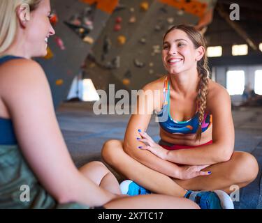 Two Women Taking A Break And Talking By Climbing Wall In Indoor Activity Centre Stock Photo